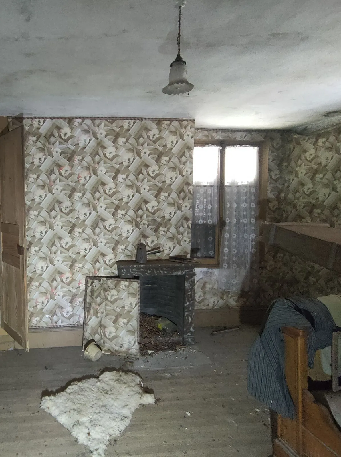 La chambre avant travaux : papier peint à fleurs, petite cheminée, plancher brut