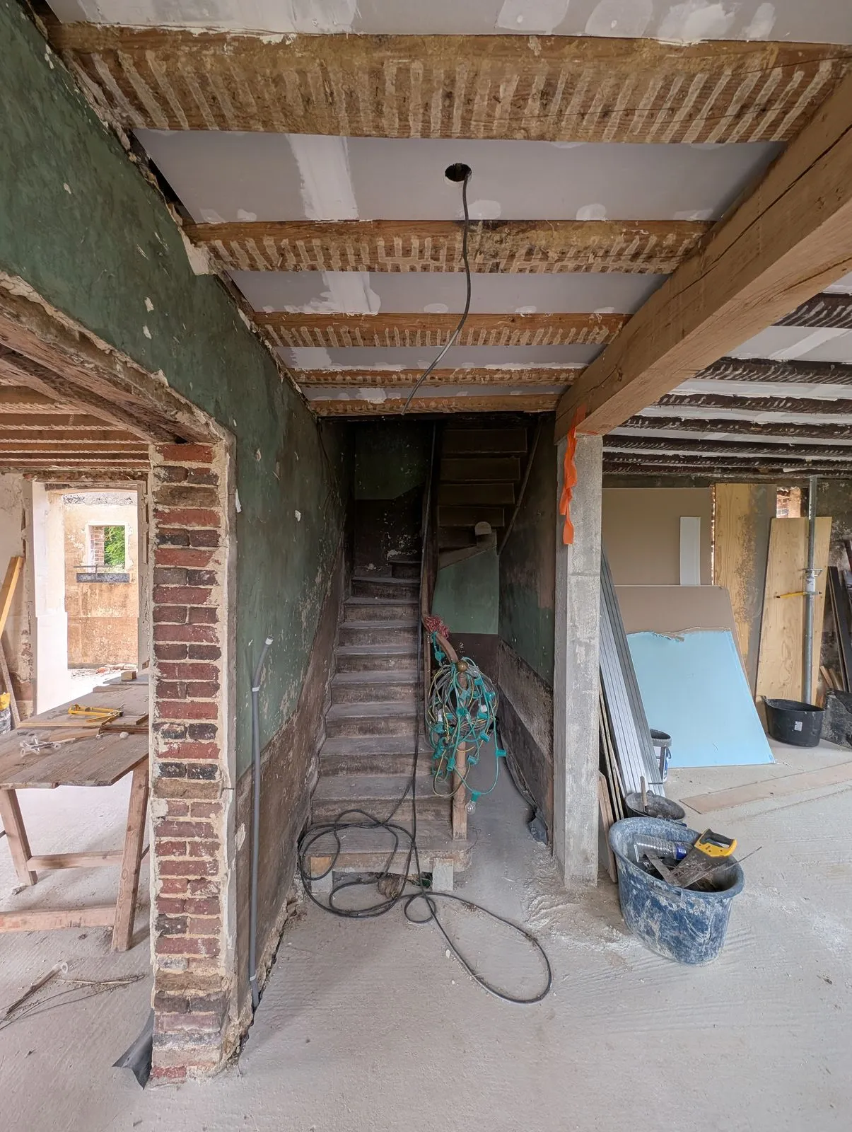 L'entrée pendant le chantier : murs en brique mis à nu, escalier d'origine au fond