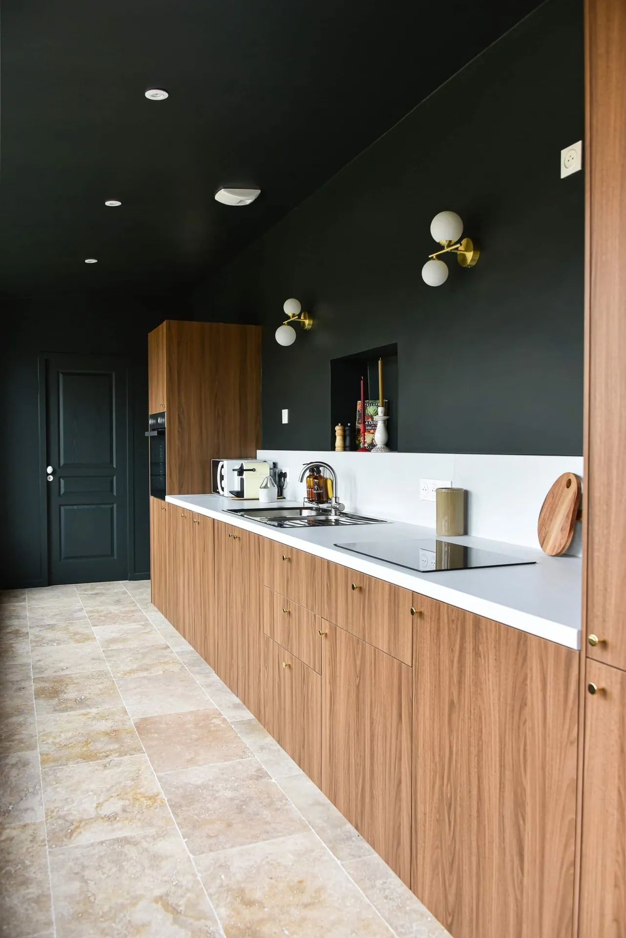 La cuisine terminée : meubles en bois, plan de travail clair, mur vert sombre et sol en pierre