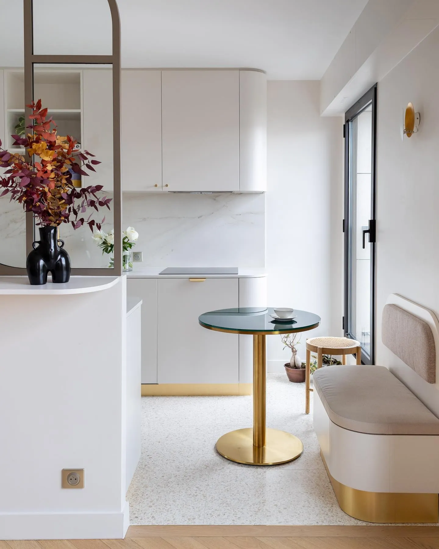 Le coin cuisine terminé : façades claires, crédence en marbre, table ronde et banquette près de la fenêtre