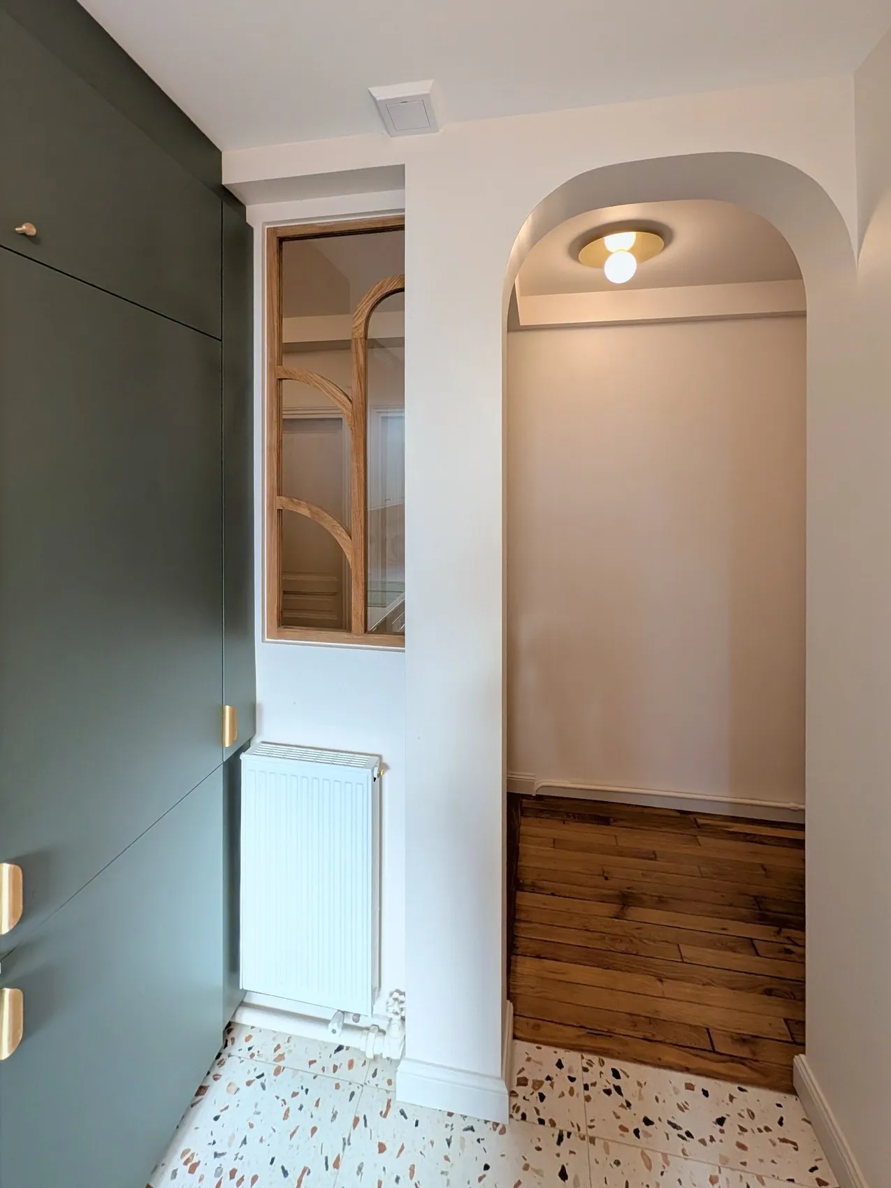 La cuisine terminée : meuble vert sauge, verrière en bois, arche vers le couloir et sol en terrazzo