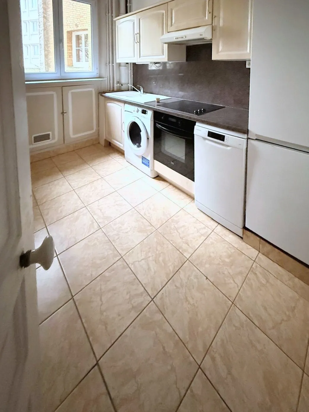 La cuisine d'origine vue depuis la porte : carrelage beige, meubles et électroménager alignés
