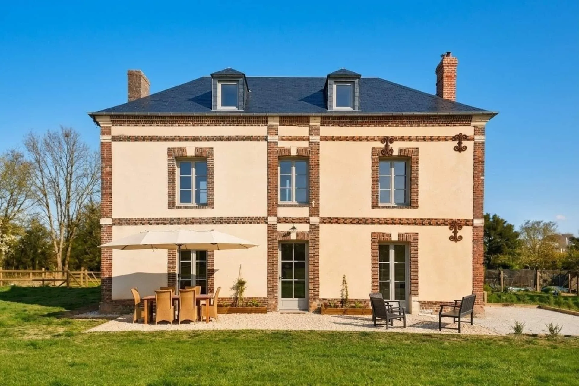 La maison de maître rénovée, vue du jardin : façade en brique et pierre, toit d'ardoise, terrasse