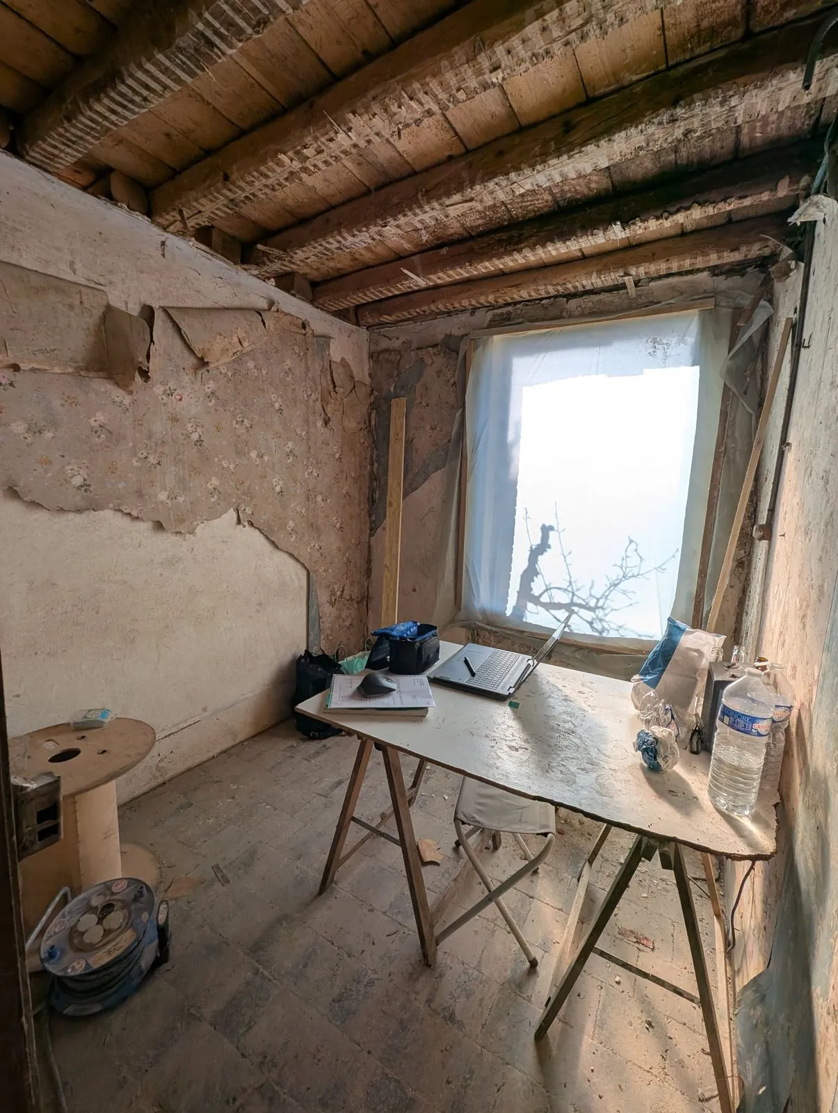 La pièce de l'étage avant travaux : enduits tombés, solives apparentes, fenêtre sur le jardin