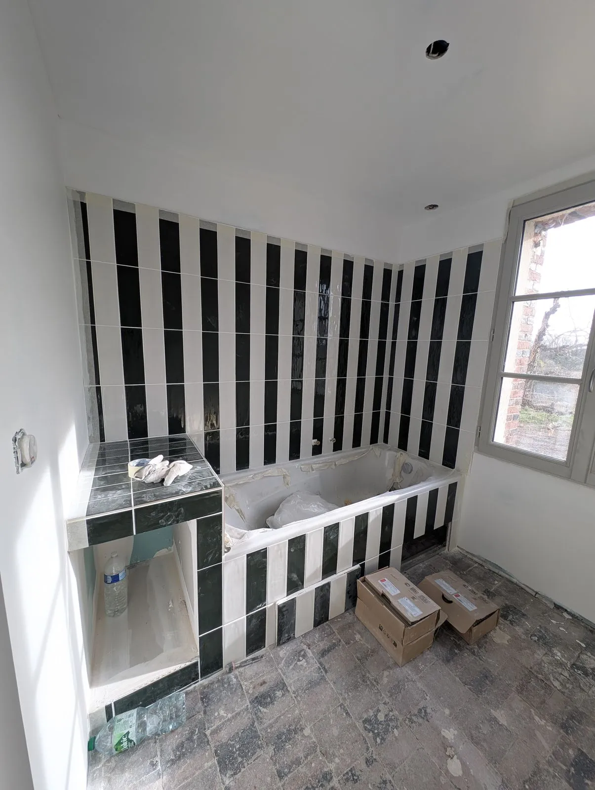 La salle de bain pendant le chantier : baignoire en place, faïence rayée en cours de pose