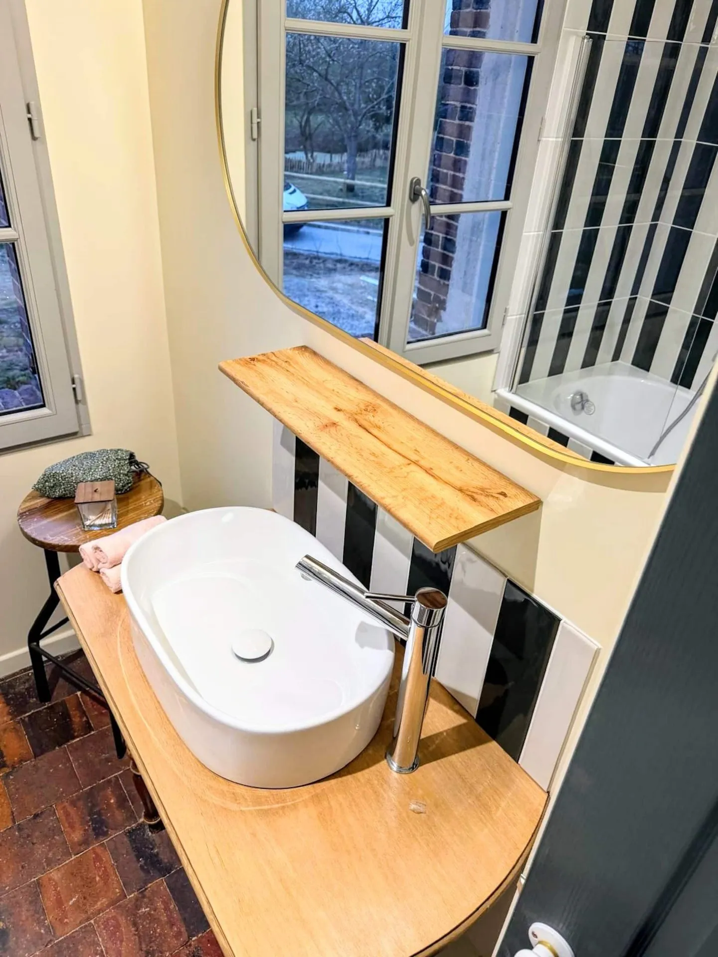 La vasque de la salle de bain, plan en bois, miroir rond et tomettes au sol