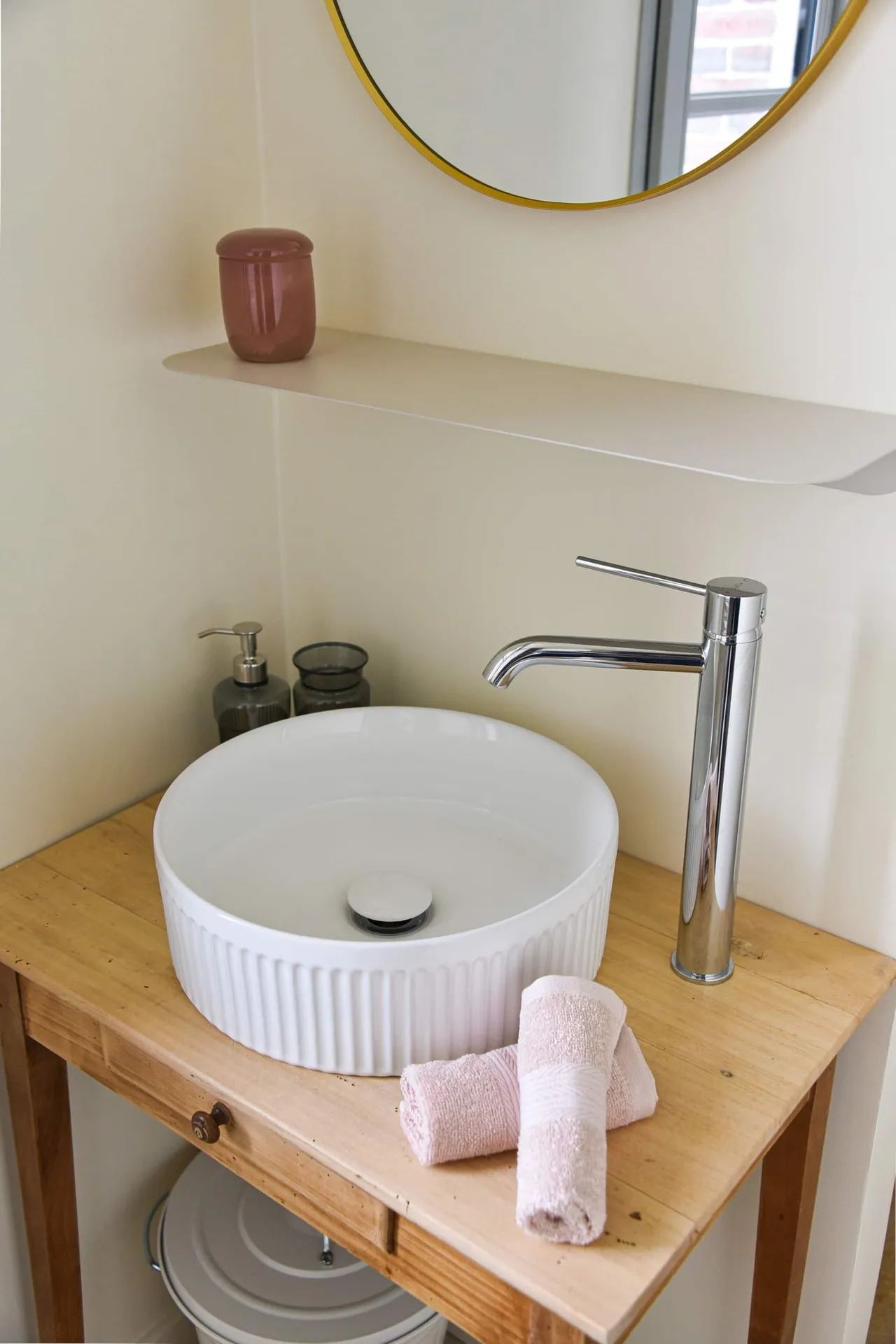 La vasque ronde de la salle de douche, sur un meuble en bois, sous un miroir doré